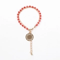Detail eines Armbandes mit roten Perlen, Goldkette und funkelndem Zirkon-Rundanhänger - Rot