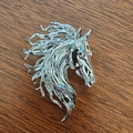 Artistic silver horse head brooch with detailed mane relief on wooden background - Silver