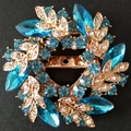 Détail macro d'une broche fleur dorée ornée de cristaux bleu clair et de strass brillants - Boucle d'Écharpe Bleu Lagon