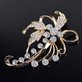 Detailed close-up of golden floral brooch with sparkling rhinestones on black background - White