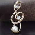 Close-up of golden treble clef brooch with shimmering rhinestones and a white pearl - Pearl Music Note