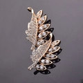 Elegante spilla a piuma dorata con cristalli scintillanti su base nera riflettente - Oro