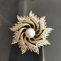 Primer plano macro de lujoso broche de molinillo dorado con perla central y circonitas brillantes - Molino de Viento Dorado