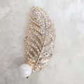 Detail der goldenen Federbrosche mit glitzernden Kristallen und einer großen weißen Perle - Gelb