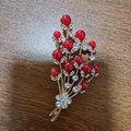Detail shot of golden floral brooch with red pearls and white rhinestones on wood - String of Red Pearls