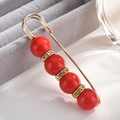 Macro shot of gold safety pin brooch with red pearls and sparkling rhinestone spacers - Pin Style / Red
