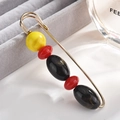 Detail of a large gold safety pin brooch featuring red, yellow and black beads - Pin Style / Yellow