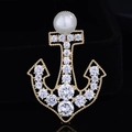 Dettaglio di una spilla ad ancora dorata con perla bianca e cristalli scintillanti - Oro