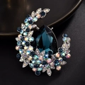 Dettaglio ravvicinato di una spilla a mezzaluna con gemma blu a goccia e strass pavé - Blu