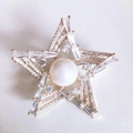 Dettaglio macro della spilla a stella con grande perla e zirconi brillanti su base dorata - Oro