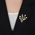 Detailopname van een elegante gouden bladbroche met witte en roze parels op een blazer - Goud