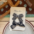 Close-up of two fabric bow hair clips with plaid and floral patterns on display card - Black Plaid Flower