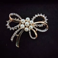 Elegant gold bow brooch featuring sparkling rhinestones and delicate white pearl center - Bow