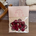 Detail von dunkelroten Plüsch-Haargummis in rosa Vintage-Verpackung auf Holztisch - Roter Bommel-Stil