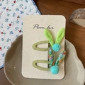 Detail view of handmade floral rabbit ear hair clips with mini pom poms on display card - Green Floral