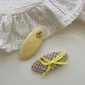 Détail d'une pince BB jaune perlée et d'un nœud à carreaux violets sur tissu dentelle - Nœud Perle Ovale Jaune