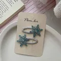 Close-up of blue glitter snowflake hair clips with diamond accents on a cream card - Blue Snowflake