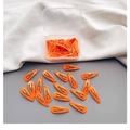 Leuchtend orangefarbene Haarclips in einer transparenten Box auf weißem Stoffhintergrund - Orange