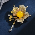 Elegante Blumenbrosche mit Bernstein-Perle und Zirkon-Quaste auf dunklem Hintergrund - Bienenwachs Blumenquaste