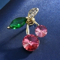 Macro shot of cherry-shaped brooch featuring pink crystals and green leaf on blue fabric - 10-Satellite Stone Cherry