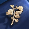 Vue détaillée de la broche feuille de ginkgo dorée avec strass blancs et pommes de pin - Branche de pin