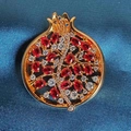 Detailansicht einer Granatapfel-Brosche mit roten Zirkonia auf blauem Seidenstoff - Ziegelrot