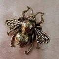Primer plano de broche de abeja dorada con alas caladas sobre tela de seda rosa - Oro Envejecido
