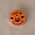 Detail of Jack-o'-lantern enamel pin with bat wings and Covid-19 Vaccinated text - Orange Red Bat