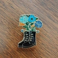 Dettaglio di una spilla smaltata con stivali neri e vivaci fiori blu su legno - Nero