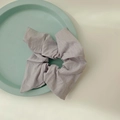 Coletero minimalista de lino violeta claro con textura plisada suave sobre bandeja - Gris Elegante