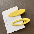 Close-up of yellow oval matte hair clips on a white card over dark brown leather - Solid And Hollow Combination / Bright Yellow