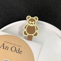Niedliche braune Bären-Haarspange in mattem Design an einer weißen Porzellanplatte - Gelber Bär