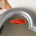 Single matte coral orange 5cm snap hair clip displayed on a silver heart-shaped mirror - Orange Red