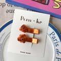 Zwei glänzende orangefarbene Haarspangen in Rosenform auf einer Displaykarte - Rosenstil / Orangefarbene Serie