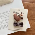 Détail d'un ensemble de pinces à cheveux fait main avec cœur et nœud sur fond de livre - Barrette Cœur Nœud Marron