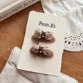 Détail de deux barrettes à nœuds en tricot marron avec perle sur un bureau en bois - Pince à Cheveux Nœud 3D Marron