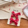 Pair of red plaid fabric bow hair clips on display card over a cozy wooden table background - Cross Knot Style (Pair)