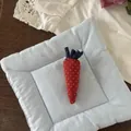 Close-up of a handmade carrot fabric brooch with blue leaves on a soft quilted cushion - Red Carrot (NK1352)