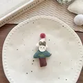 Macro shot of a handmade knitted Christmas tree brooch with colorful pom-poms on ceramic plate - Green Christmas Tree Brooch