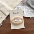 Detail von Plüsch-Lammwolle-Haarspange mit handgefertigtem Etikett auf Dekorkarte - Beigefarbener Plüsch-Haarclip mit Buchstaben