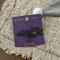 Nahaufnahme schwarzer Glitzerstern-Haarspangen auf violetter Karte auf grober Leinwand - Schwarzer Stern