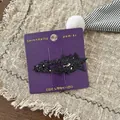 Close-up of black glitter star hair clips on a purple display card over rustic burlap - Black Star
