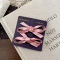 Detail of pink satin bow hair clips on a purple display card with silk texture - Pink