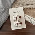 Gros plan de deux pinces à cheveux ours en peluche avec nœuds sur carte de présentation - Pince à Cheveux Ours Blanc Crème