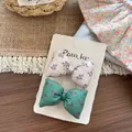 Detalle de pinzas para el pelo con lazos de tela floral para niñas sobre fondo de madera - Pinza para el Pelo con Lazo de Capullo