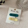 Close-up of two matte oval BB hair clips in dark green and pastel yellow on a paper card - Dark Green And Off White Oval Style