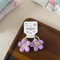 Nahaufnahme von lila Stoffblumen-Haargummis mit gelben Perlen auf Holztablett - Lila