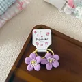 Close-up of handmade purple floral hair ties with yellow beads on a wooden tray - Purple
