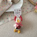 Détail d'un chouchou canard en peluche avec nœud rouge et broderie fleurie sur fond doux - Style Canard à Foulard Beige