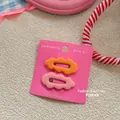 Detail view of wavy candy-colored hair clips in pink and orange on a display card - Orange and Pink